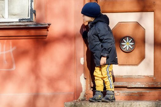 A cute little boy dressed in autumn is going for a walk in the old city with a hat.