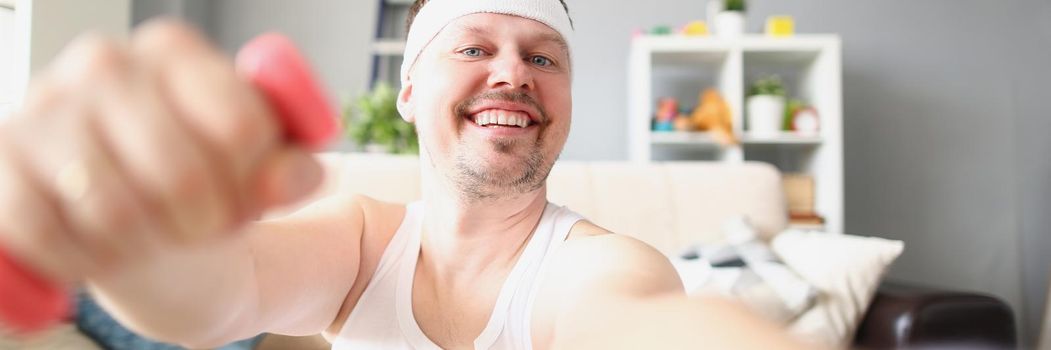Portrait of smiling middle aged man lifting dumbbells and taking selfie on smartphone. Record progress on device, follow goal. Sport, weight loss concept