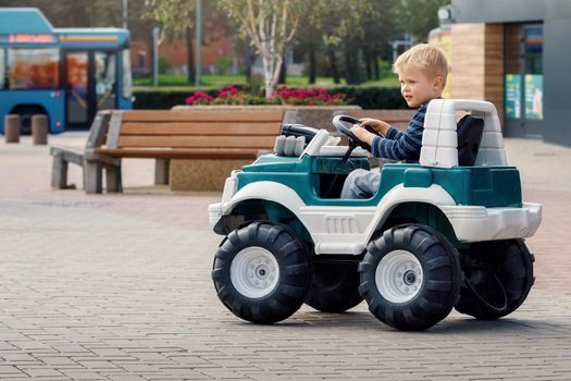 Little preschool kid boy driving big toy car and having fun outdoors. Child enjoying warm summer day in city landscape.