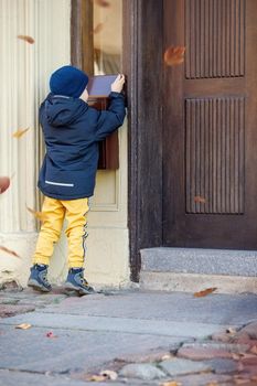 Little boy, checking the mail in outdoors mailbox. The kid is waiting for the letter, checks the correspondence and looks into the metal mailbox. Falling leaves during the autumn season.
