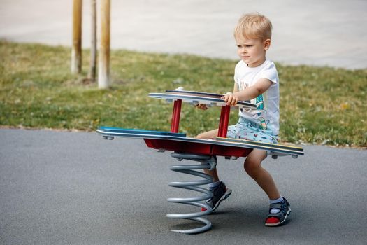 A little boy in a white T-shirt balances on a swing with a big mainspring.