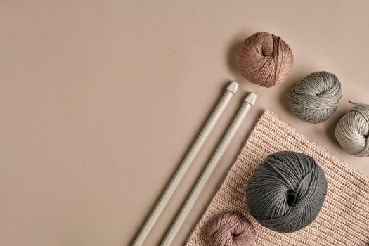 Knitted from a gray yarn sweater and thread for knitting closeup. Knitting as a hobby. Accessories for knitting on a beige background. Top view. Still life. Copy space. Flat lay
