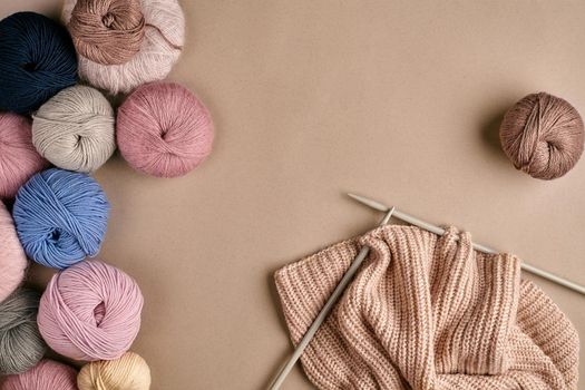Set of colorful wool yarn and knitting on knitting needles on beige background. Knitting as a kind of needlework. Colorful balls of yarn and knitting needles. Top view. Still life. Copy space. Flat lay