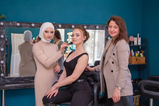 A makeup artist paints the skin of a girl's face with a brush in the salon. Female master makes makeup to a young woman. Business concept - beauty salon, facial skin care, cosmetology.