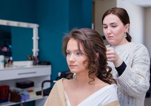 The face of a client girl, behind the master is styling her hair. The hairdresser makes a hairstyle for a young woman. Barber shop, business concept. Beauty salon, hair care.