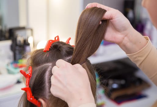 Close-up of the master's hand making a loop of hair on a woman's head. The hairdresser makes a hairstyle for a young woman. Barber shop, business concept. Beauty salon, hair care.