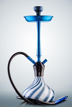 Modern hookah on light grey background. Eastern smokable water pipe smoking. Hookah with black rubber tube and blue and white flask on light grey background. Still life.