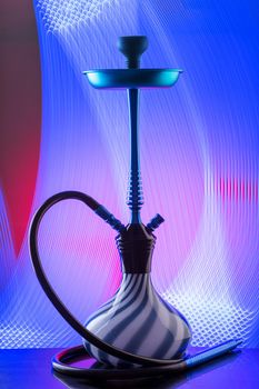 Modern hookah on colorful background. Eastern smokable water pipe smoking. Hookah with black rubber tube and blue and white flask on interesting colorful background. Still life.