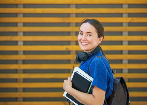 student girl is standing near wooden wall holding books