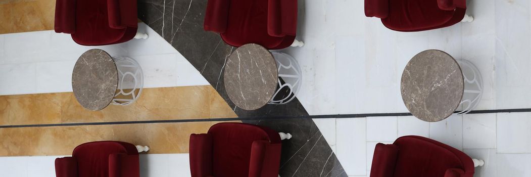Soft burgundy armchairs and tables standing in hotel lobby top view. Interior design concept