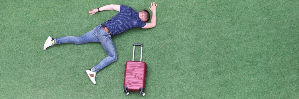 Man with suitcase lying on green grass top view. Travel and vacation concept