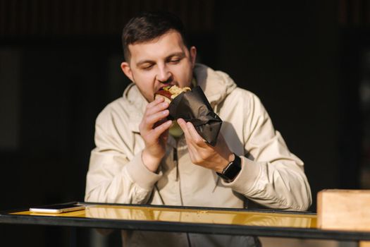 Handsome man having traditional hot dog cuisine during rest break. Caucasian guy enjoying street cuisine outdoor. Male eating unhealthy fast food.