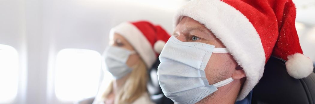 Man and woman in protective masks and santa hats flying in airplane. New year holidays during covid19 pandemic concept
