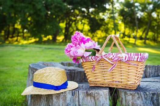Beautiful basket with flowers and hat stands on a wooden stump
