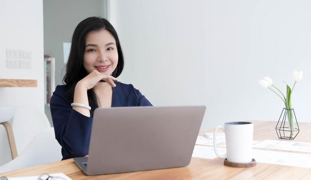 Charming Asian woman working at the office using a laptop Looking at the camera..