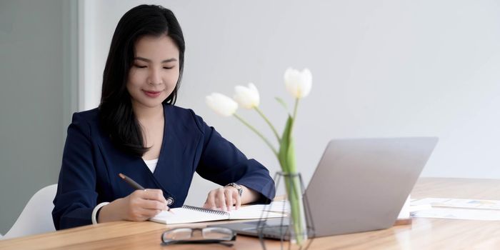 Happy young asian businesswoman sitting on her workplace in the office. Young woman working at laptop in the office..