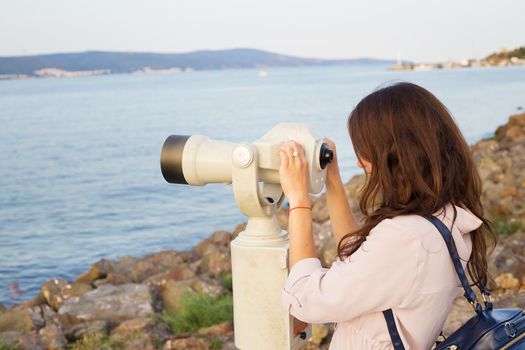 The girl looks through the telescope at the sea.