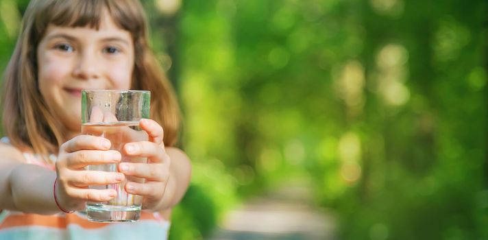 A child drinks water from a glass on the nature. Selective focus. Drink.