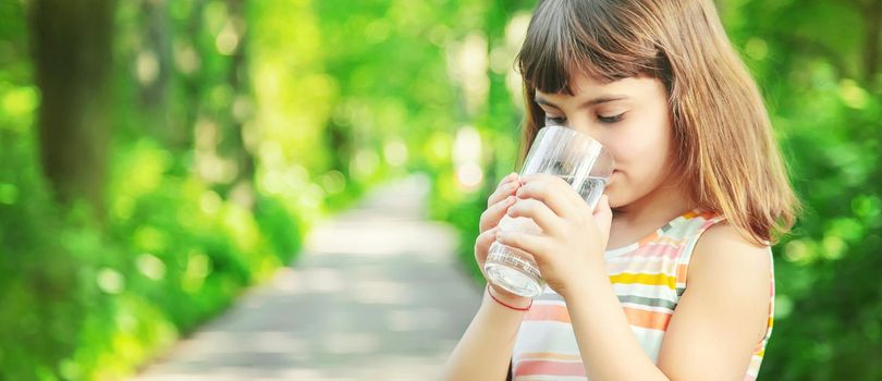 A child drinks water from a glass on the nature. Selective focus. Drink.