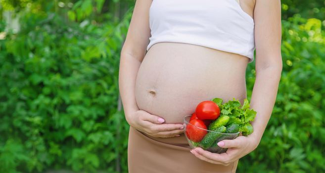 A pregnant woman with vegetables in her hands. Selective focus. food.