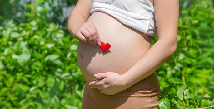 Pregnant belly and heart in hands. Selective focus. people.
