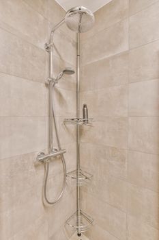 Shower faucets attached to tiled wall near glass partition and ornamental curtail in washroom at home