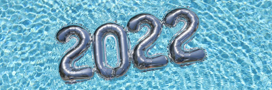 Helium balloons with numbers 2022 lying on water in swimming pool top view closeup background. New year holiday planning concept