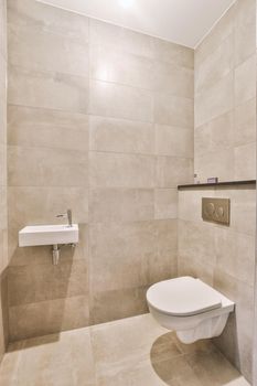 Wall hung toilet and small sink in corner in lavatory room with beige tile