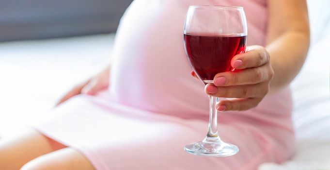 A pregnant woman is drinking wine. Selective focus. people.