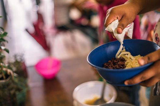 Closeup on the hand of a Latin woman serving sour cream on a plate of rice and beans, traditional Nicaraguan food for breakfast and school snack