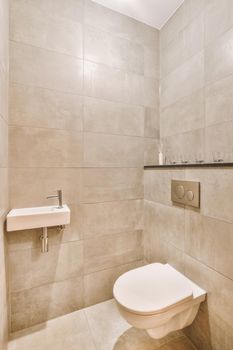 Wall hung toilet and small sink in corner in lavatory room with beige tile