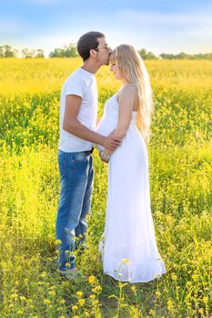 Pregnant woman and man photo shoot in mustard field. Selective focus.