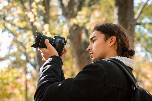 Photographer looking at screen of his camera, shooting landscapes of autumn forest