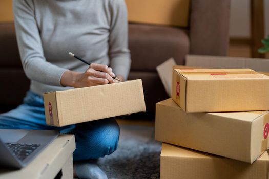 Shipping shopping online ,young start up small business owner writing address on cardboard box at workplace.small business entrepreneur SME or freelance asian woman working with box at home