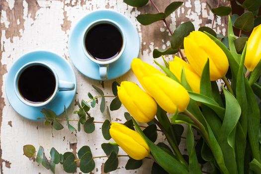 two blue cup of coffee with yellow tulips on old table