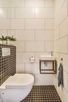 Modern flush toilet and ceramic sink installed on white tiled walls near mirror and towel in small restroom at home