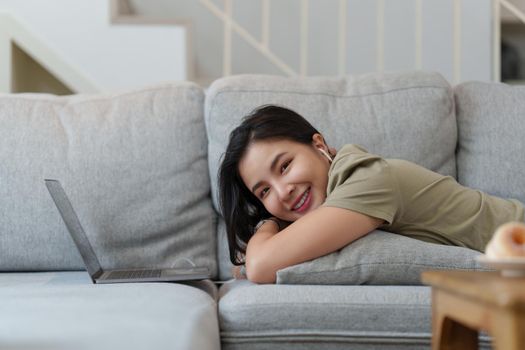 Portrait of Happy Beautiful woman lay down on cozy couch and listen music by streaming on laptop