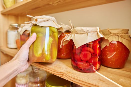 Storage of food in the kitchen in pantry. Pickled canned vegetables and fruits on the shelf, jar of cucumbers close-up. Cooking at home, homemade preservation, household