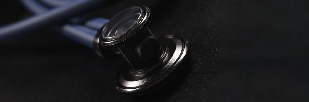 Head of medical stethoscope lying on black background closeup. Health care concept