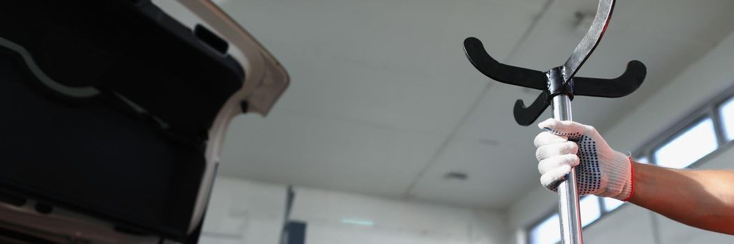 Close-up of repair service worker hold metal stand near open automobile hood. Garage with parking for fixing damaged cars. Maintenance, pit stop concept