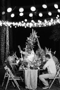 evening wedding family dinner in the forest with light bulbs and candles