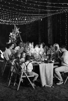 evening wedding family dinner in the forest with light bulbs and candles