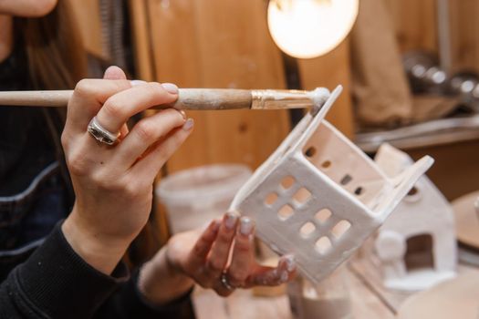 A master ceramist holds a clay product in his hands. Making a ceramic candle holder from clay. The process of coating the candlestick with glaze. Close-up.