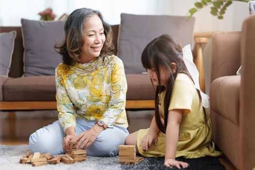 Happy moments of Asian grandmother with her granddaughter playing jenga constructor. Leisure activities for children at home