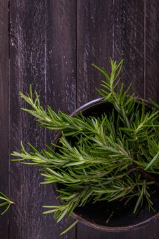 Bowl of rosemary on wooden background, top view.