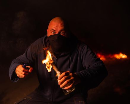 A masked man is holding a burning bottle. Molotov cocktail