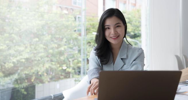 Charming Asian woman working at the office using a laptop Looking at the camera..