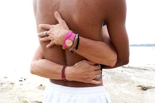Cropped photo of the hands of a caucasian woman embracing the body of an asian man on a beach