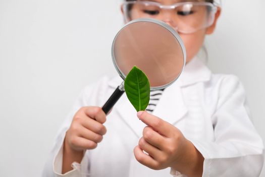 Portrait of a little girl in glasses holding a magnifying glass looking at leaves in researcher or science uniform on white background. Little scientist.