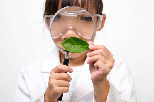 Portrait of a little girl in glasses holding a magnifying glass looking at leaves in researcher or science uniform on white background. Little scientist.